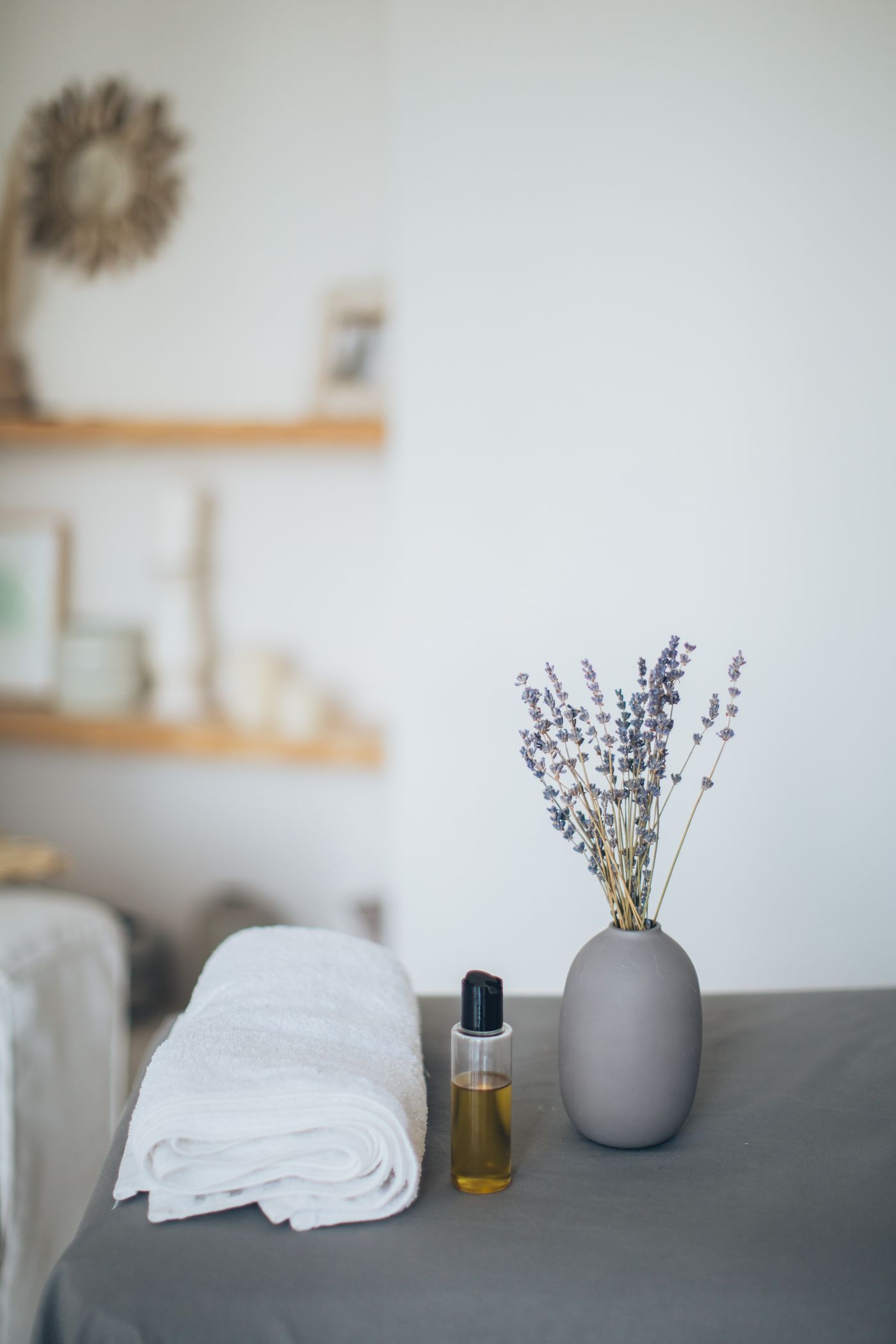 Massage oil, a folded white towel and lavender in a ceramic vase