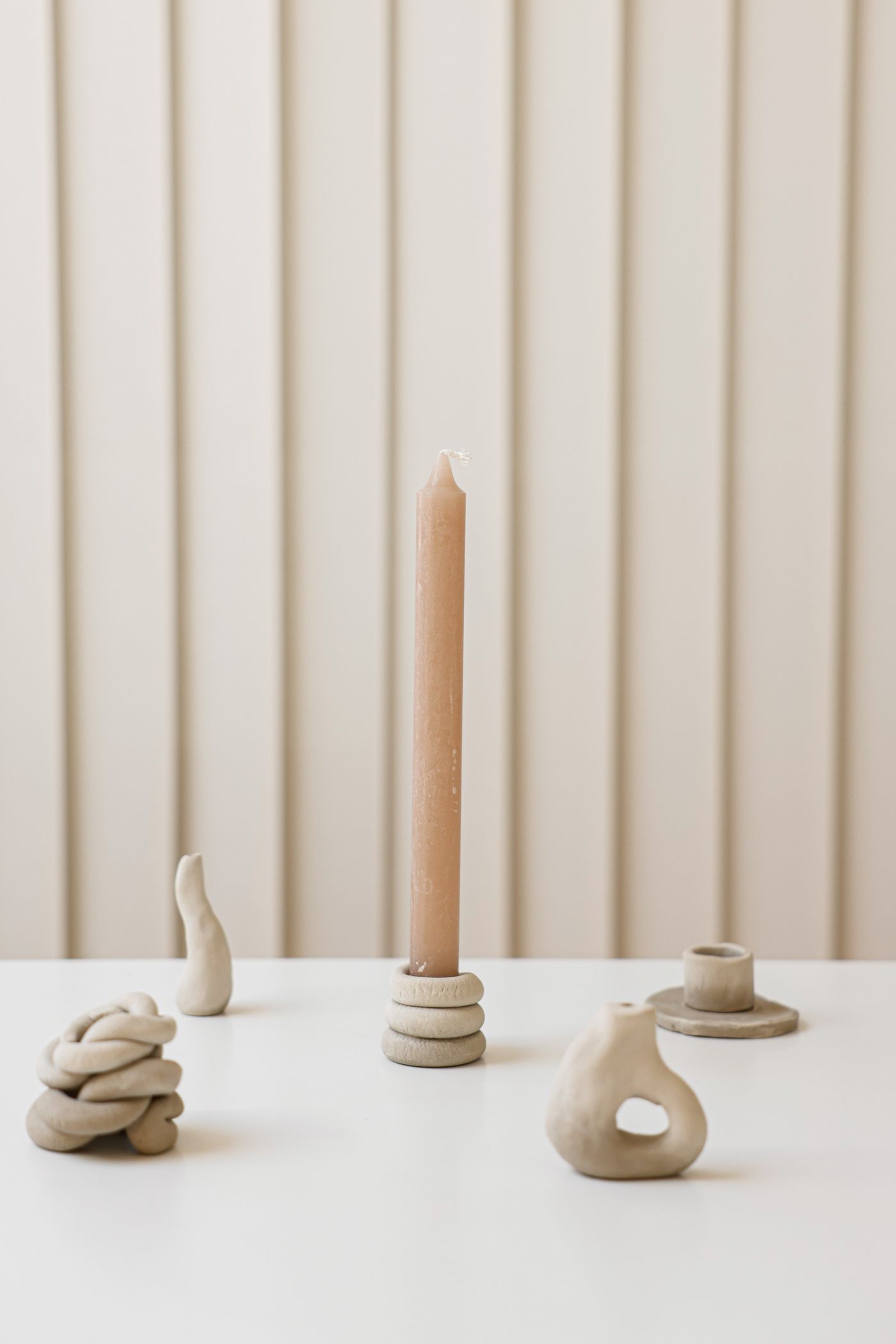 A warm beige candle with sculptural clay candleholders